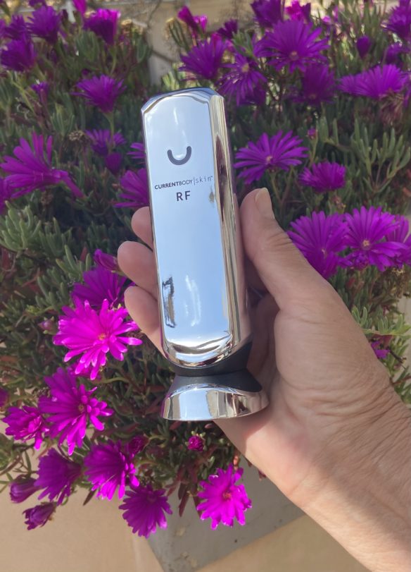 CurrentBody-Radiofrequenzgerät in der Hand vor violetten Blumen